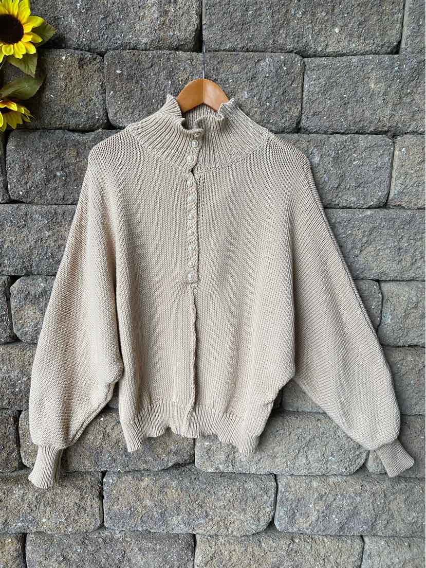 Tan oversized knit sweater with high neck and buttoned placket, ribbed cuffs and hem.