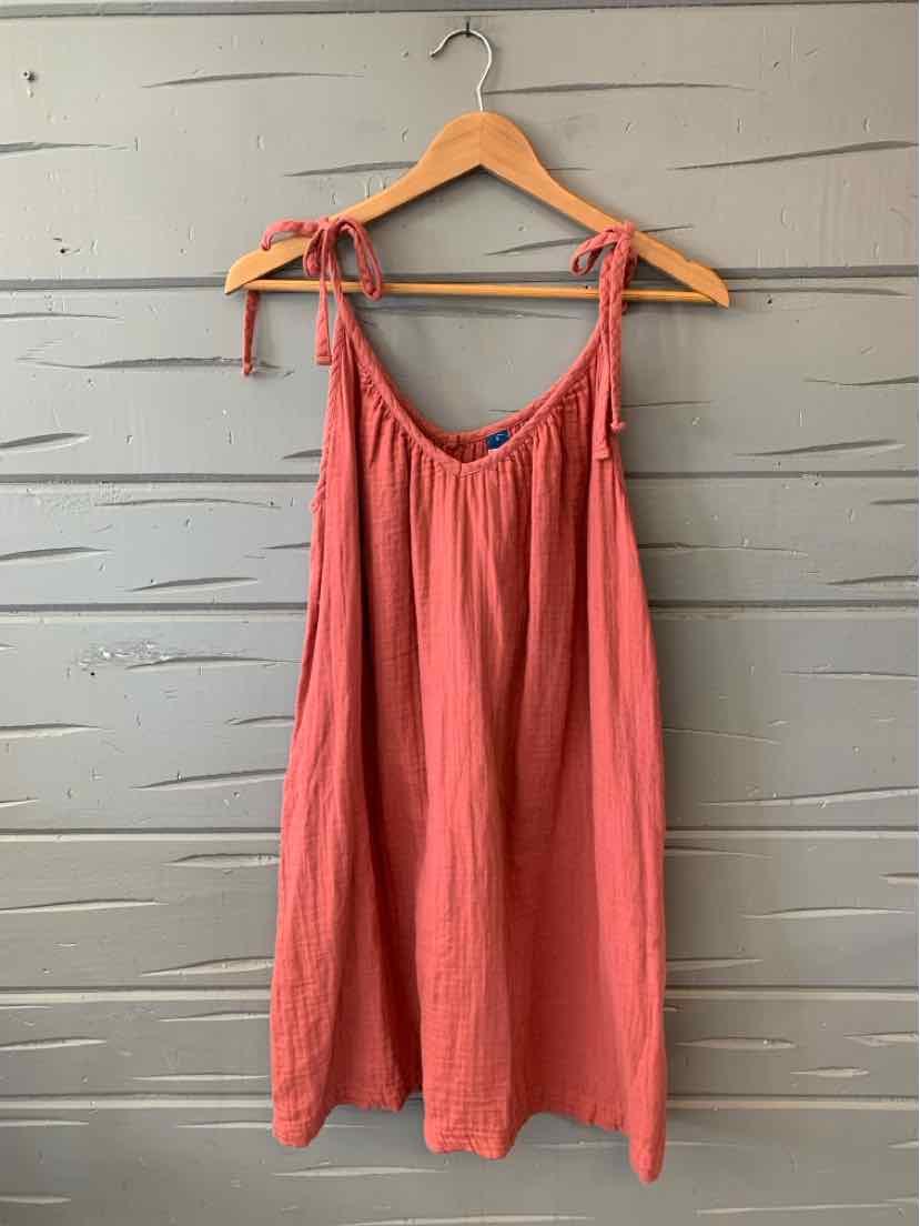 Brick red sleeveless dress with adjustable tie straps and loose, flowy fit on wooden hanger.