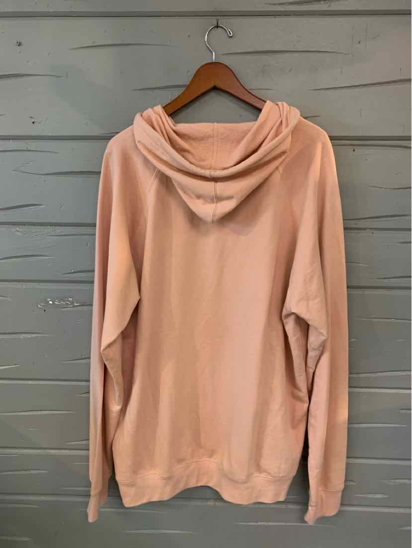 Light pink oversized hoodie with long sleeves and a relaxed fit hanging on a wooden hanger.