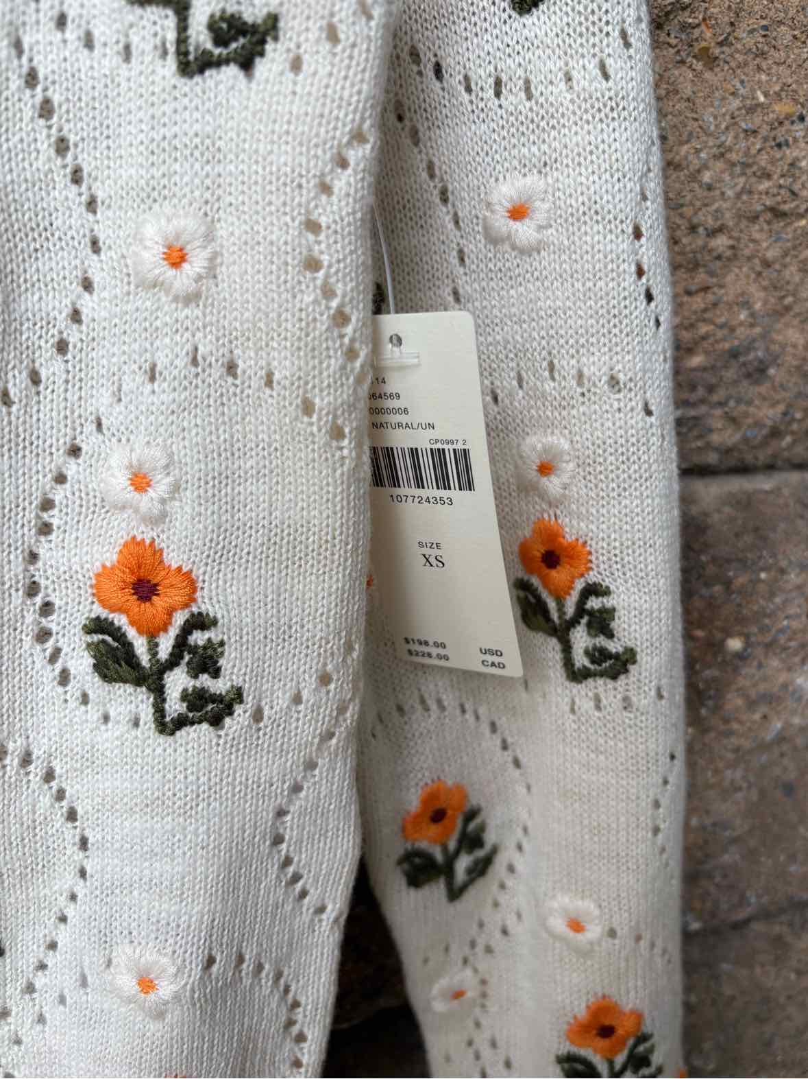 White eyelet knit fabric with embroidered orange flowers, dark green leaves, and small orange accents.