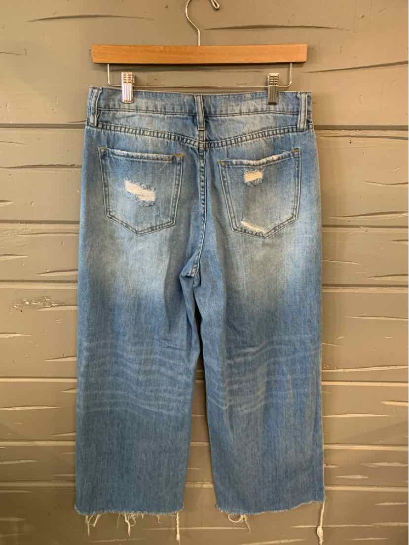 Light wash denim jeans size 5 with distressed back pockets and raw hem detailing hanging on wooden hanger.