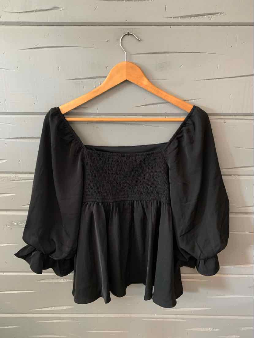 Black off-shoulder blouse with smocked bodice and billowy three-quarter sleeves on wooden hanger.