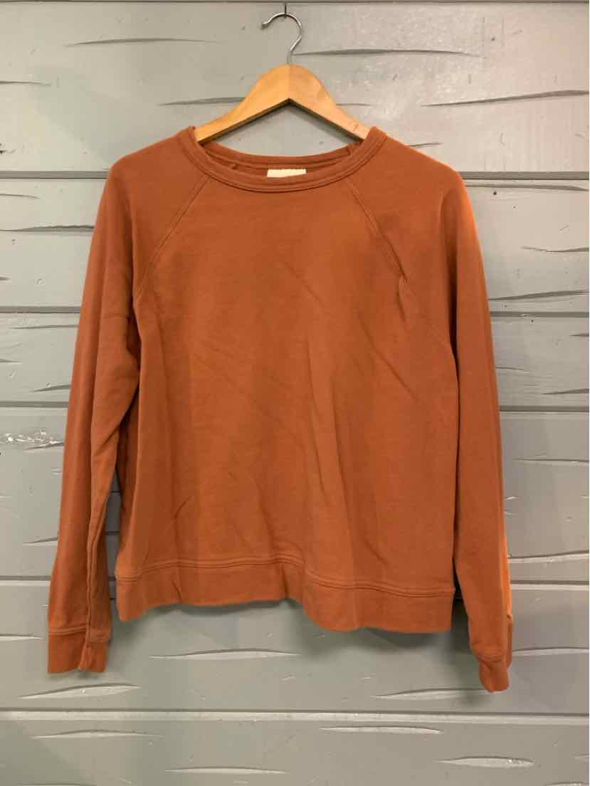 Rust orange long-sleeve crewneck sweatshirt with ribbed cuffs and hem, hanging on wooden hanger.