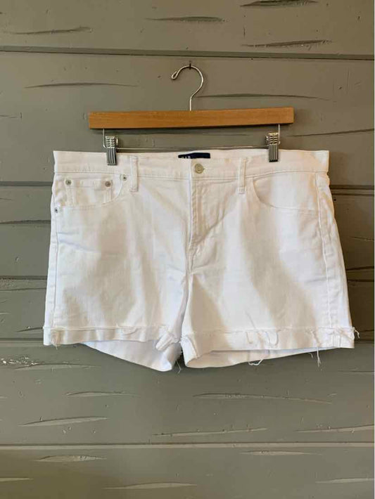 White denim shorts with cuffed hems and front pockets hanging on wooden hanger against gray wooden wall.