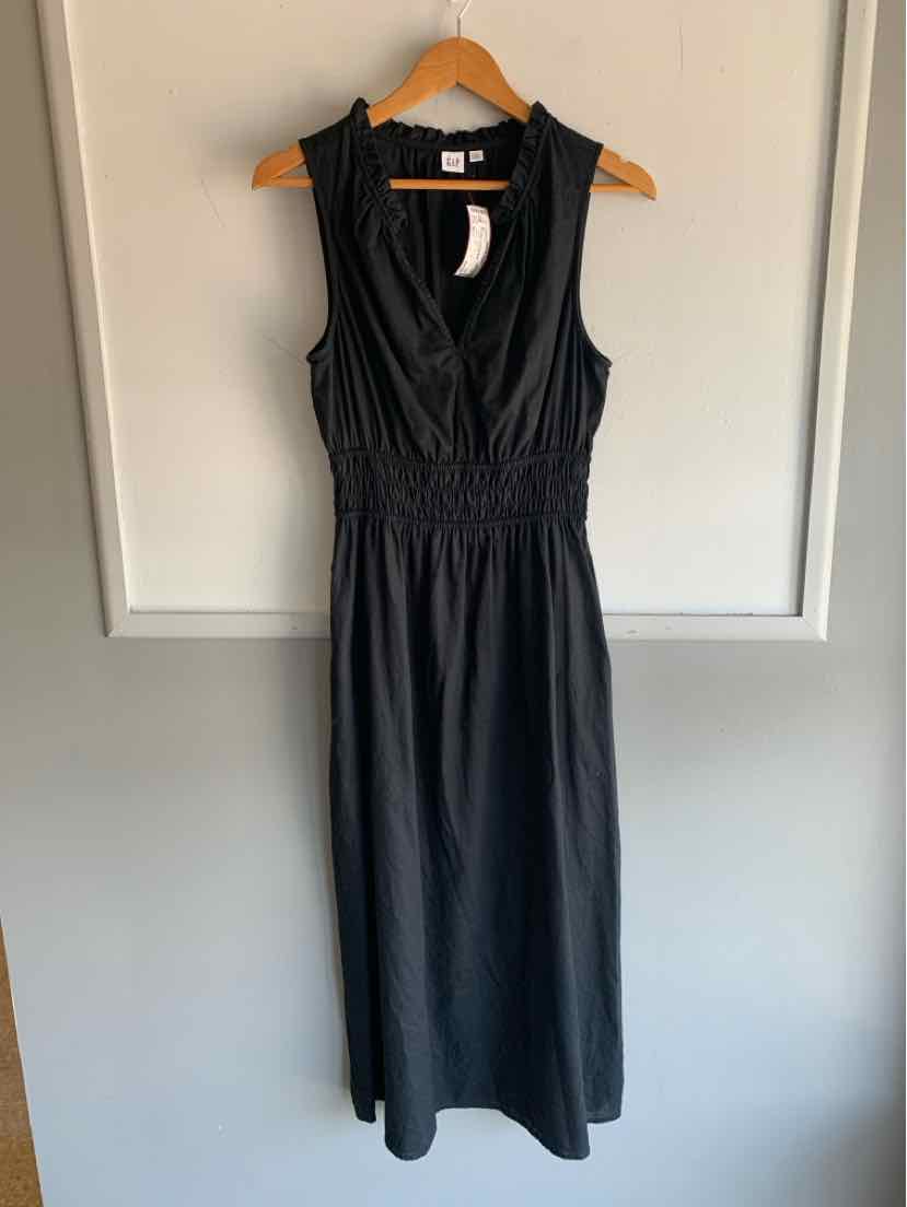 Black sleeveless midi dress with V-neck and gathered waist hanging on wooden hanger.