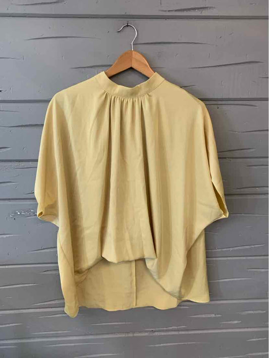 Light yellow oversized blouse with gathered neckline and high-low hem on wooden hanger.