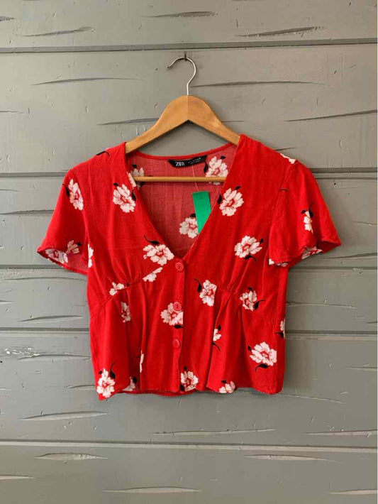 Red short-sleeve cropped blouse with white floral print and ruched front detail.