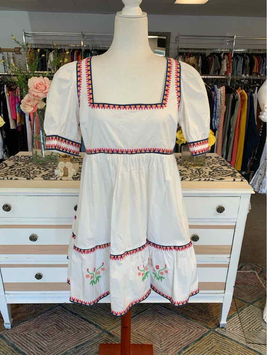 White cotton dress with puff sleeves, square neckline, and red and blue embroidered trim and floral details.