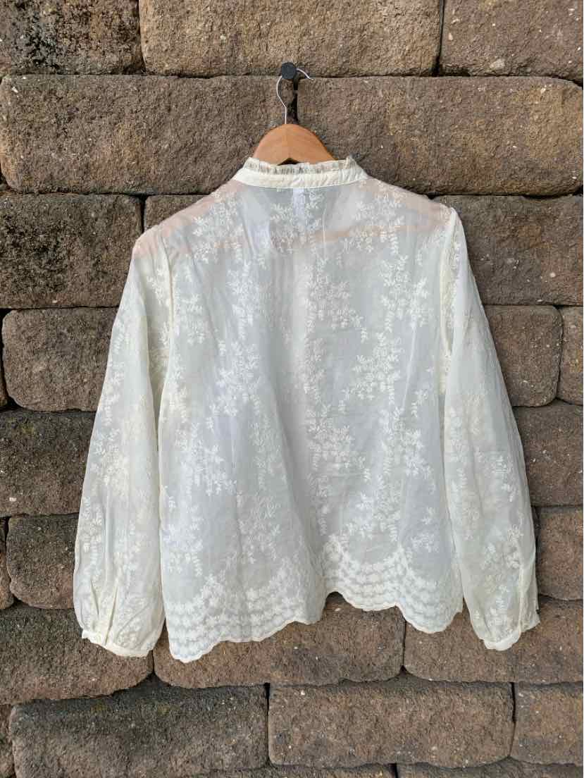 White long-sleeve blouse with floral lace pattern and scalloped hem.