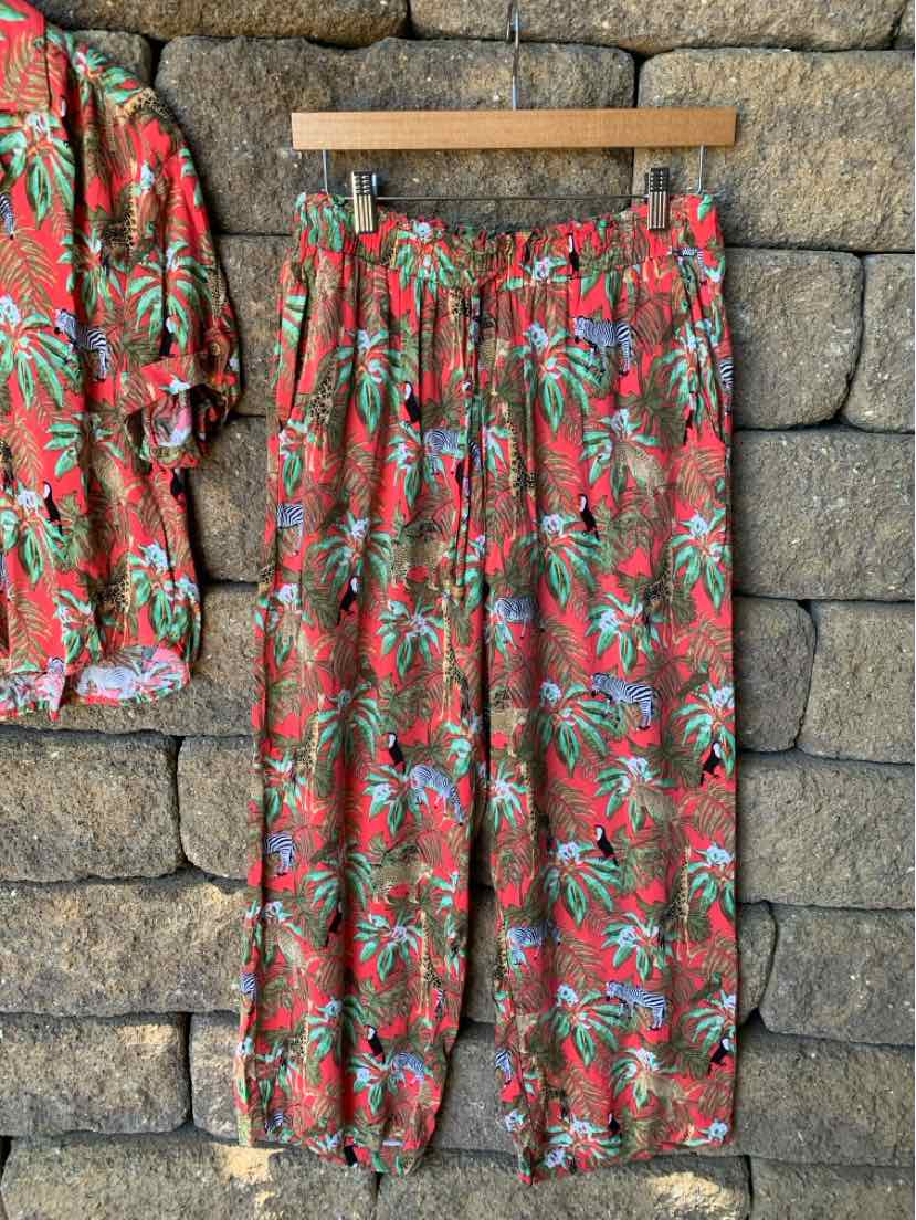 Red wide-leg pants with elastic waistband and tropical jungle print in green, blue, and beige on lightweight fabric.