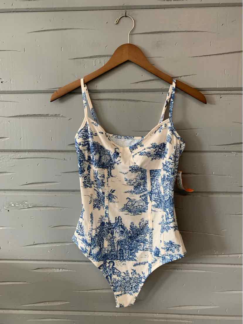 White one-piece swimsuit with blue toile print and adjustable thin straps hanging on wooden hanger.