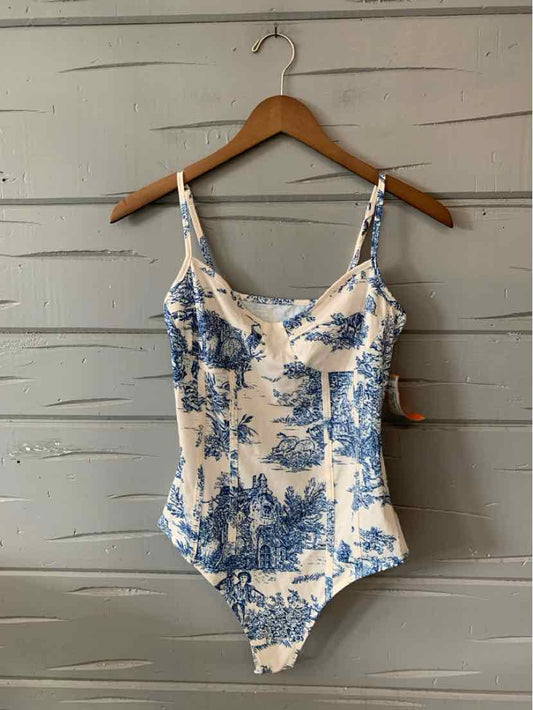 White one-piece swimsuit with blue toile print and adjustable thin straps hanging on wooden hanger.