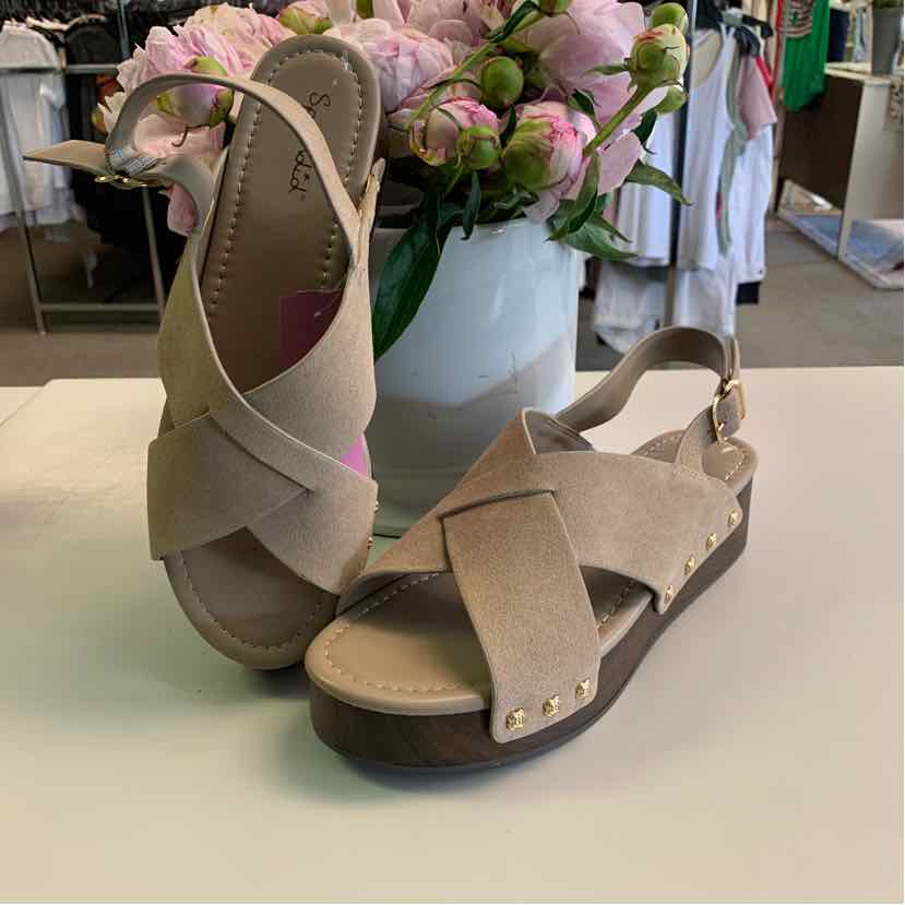 Taupe suede sandals with crisscross straps, adjustable ankle strap, and gold-tone studs on brown sole.