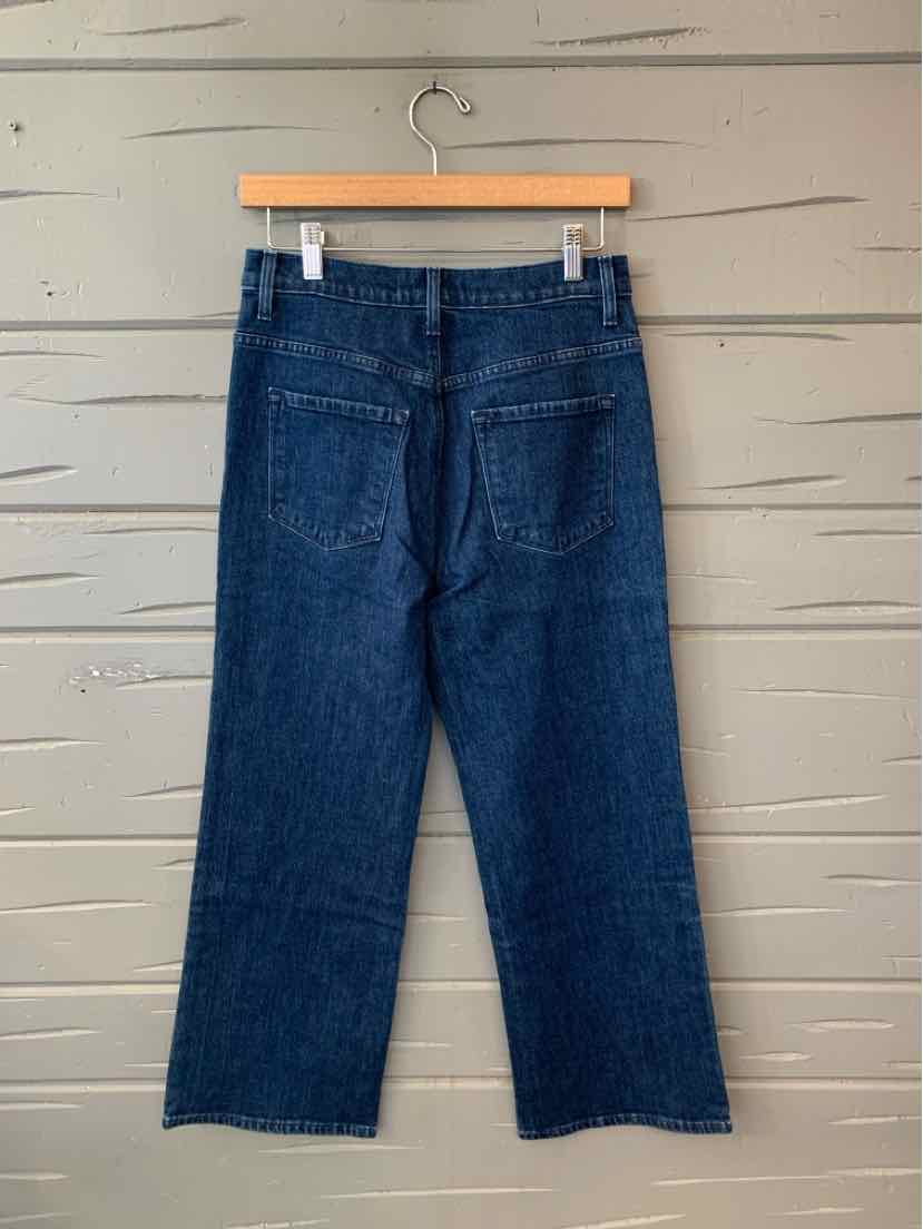 Dark blue J Brand denim jeans with a straight-leg fit and classic five-pocket styling, hanging from a wooden hanger.