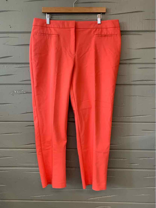 Coral-colored slim-fit trousers with front darts and a flat waistband hanging on wooden hanger.
