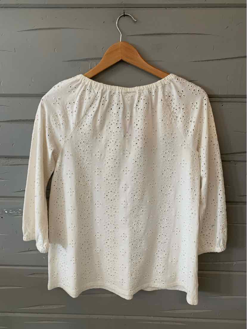 White eyelet fabric blouse with 3/4 sleeves and a round neck on wooden hanger.