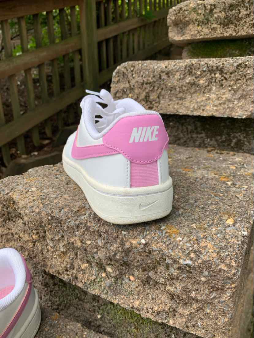 White Nike sneaker with bright pink heel panel and swoosh, resting on a stone step.