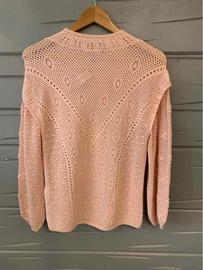Light pink knit sweater with intricate openwork pattern and long sleeves hanging on wooden hanger.