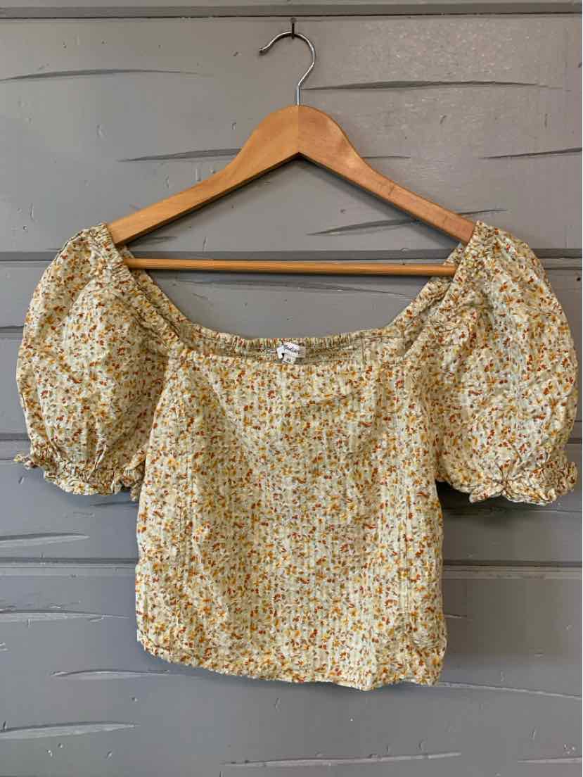Tan floral off-shoulder blouse with puff sleeves and smocked neckline on wooden hanger.