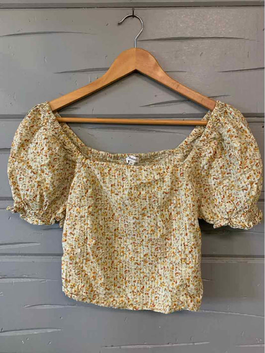 Tan floral off-shoulder blouse with puff sleeves and smocked neckline on wooden hanger.