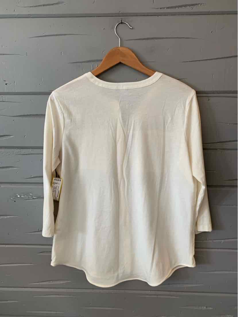Cream-colored long-sleeve shirt with a rounded hem on a wooden hanger against a gray wooden wall.