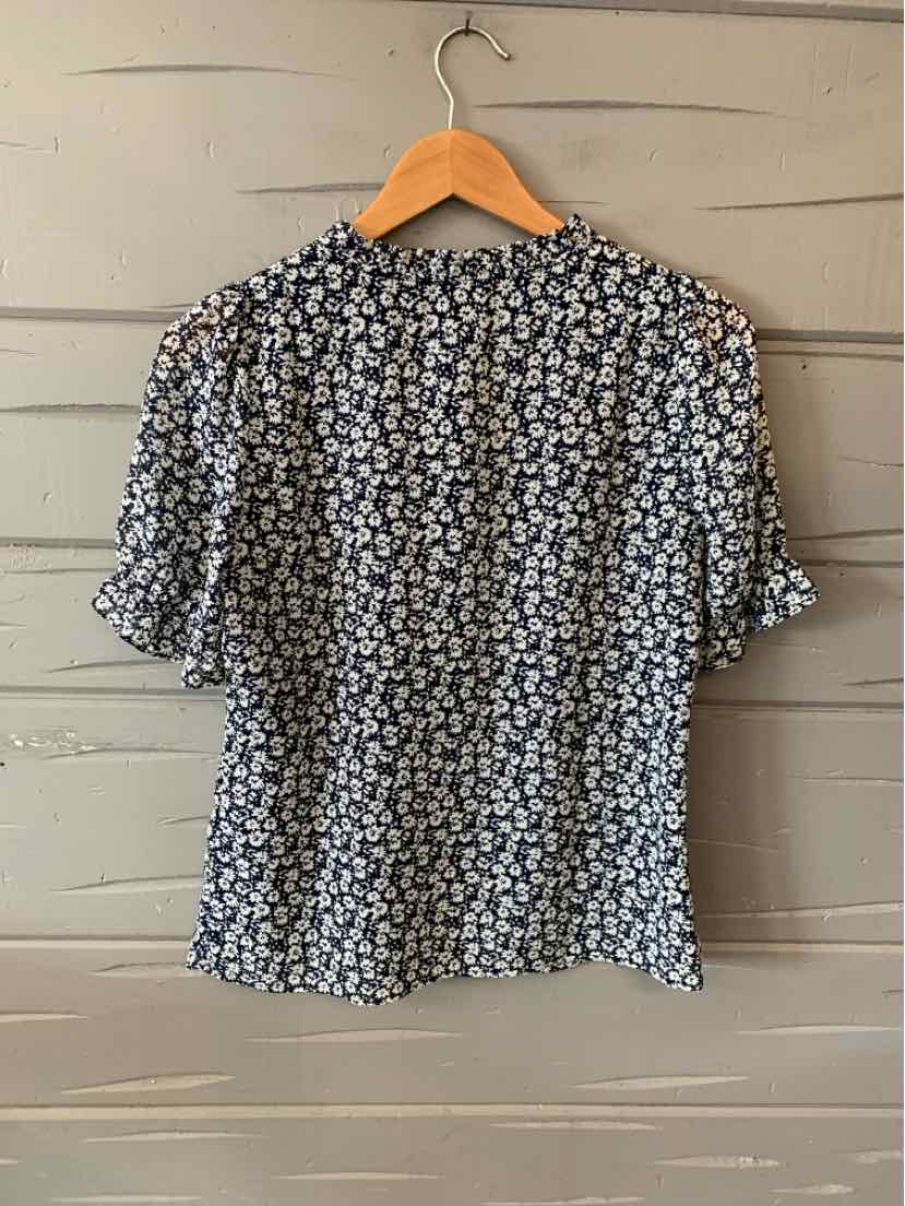 Black short-sleeve blouse with small white floral print and slightly loose fit on wooden hanger.