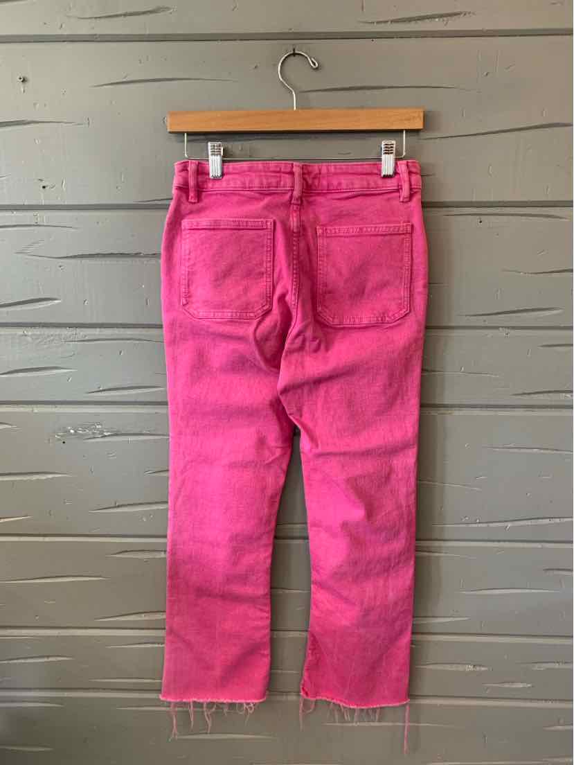 Bright pink denim jeans with a raw hem and two back pockets hanging on a wooden hanger.