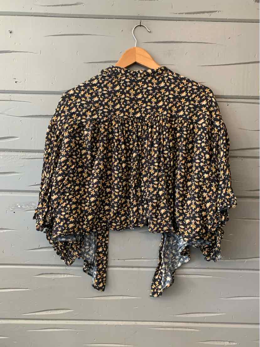 Black floral cropped blouse with loose sleeves and tie detail at the back on wooden hanger.