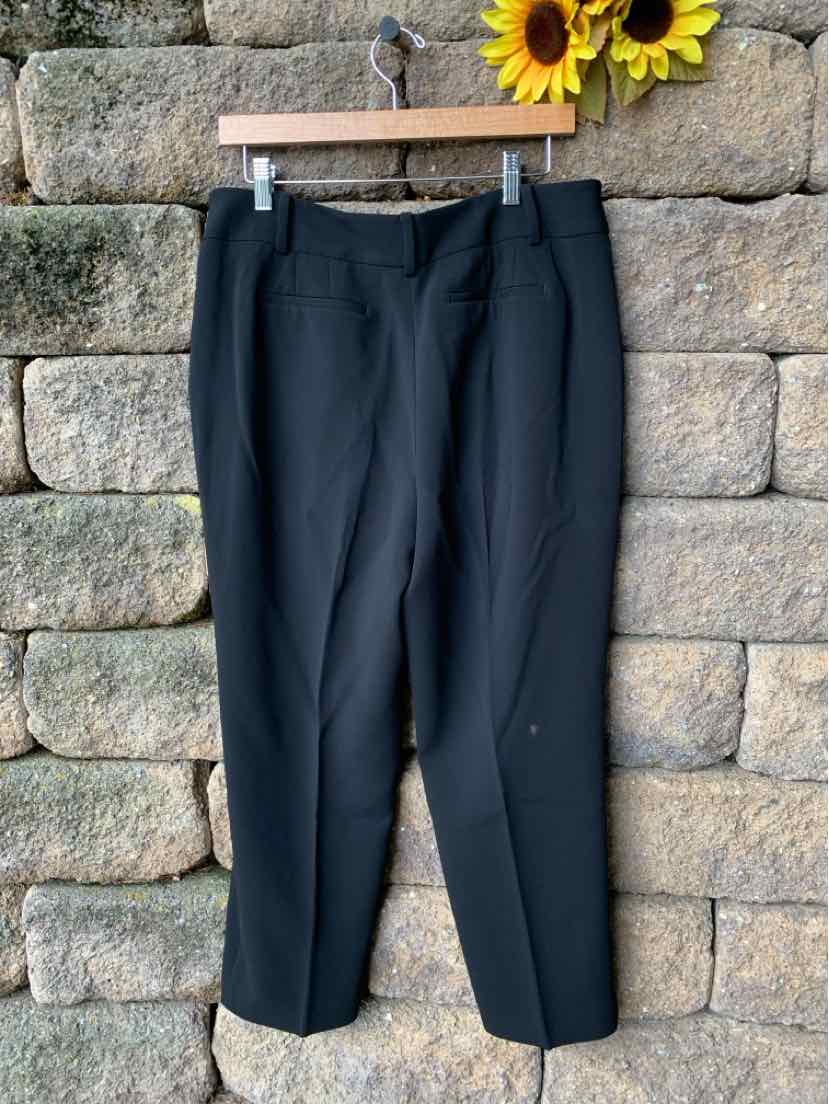 Black cropped tailored pants with belt loops, flat front, and slim fit on wooden hanger against stone wall background.