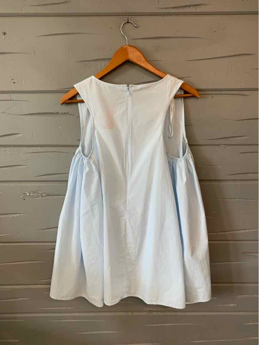 Light blue sleeveless blouse with wide armholes and loose, flared fit hanging on wooden hanger.