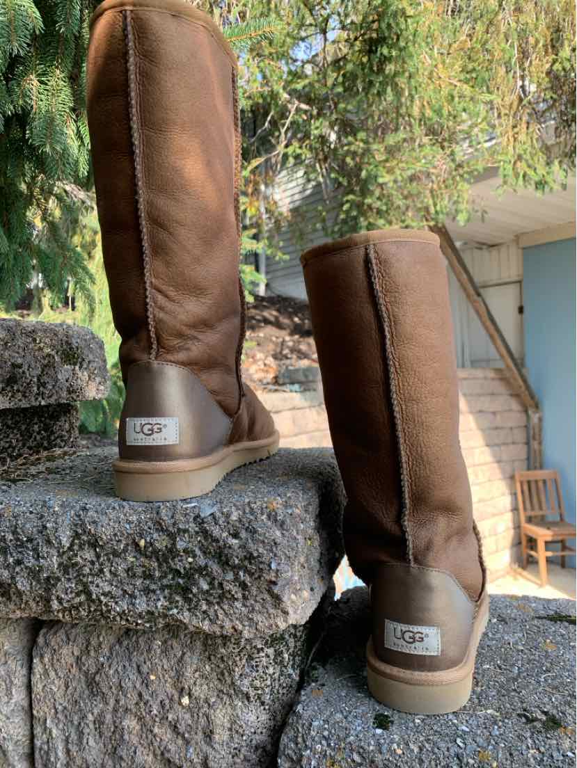 Pair of brown UGG boots with tall suede shafts, shearling lining, stitched seams, and rubber soles.