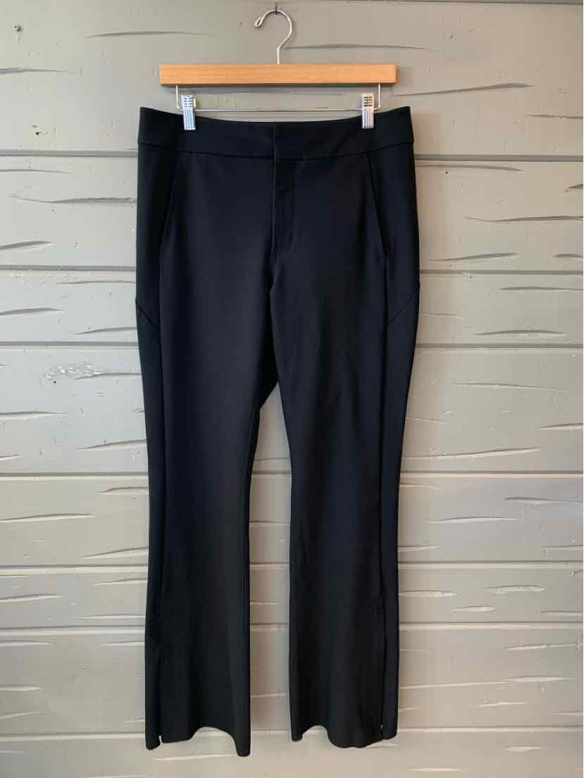 Black straight-leg pants with a mid-rise waist and smooth fabric hanging on a wooden hanger against a gray wood-paneled wall.