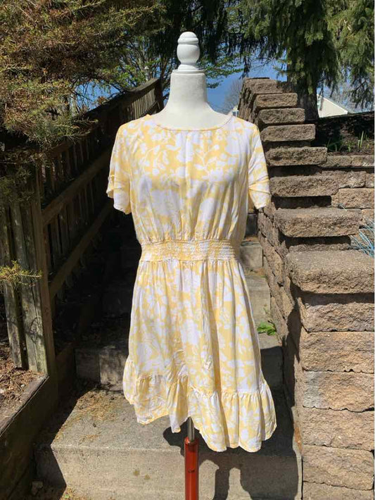 Yellow and white floral short-sleeve dress with cinched waist and ruffled hem on mannequin outdoors.