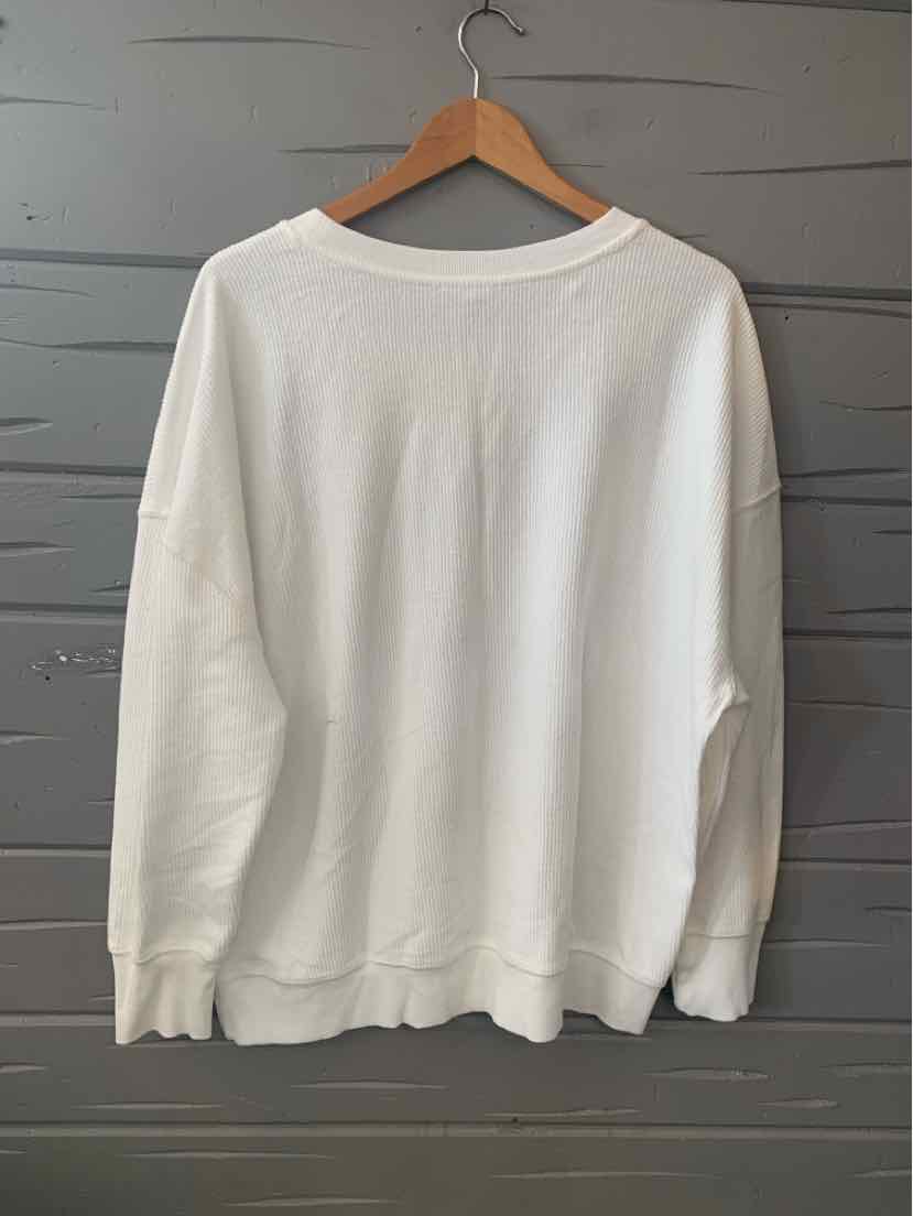 White oversized sweatshirt with ribbed cuffs and hem hanging on wooden hanger against gray wall.