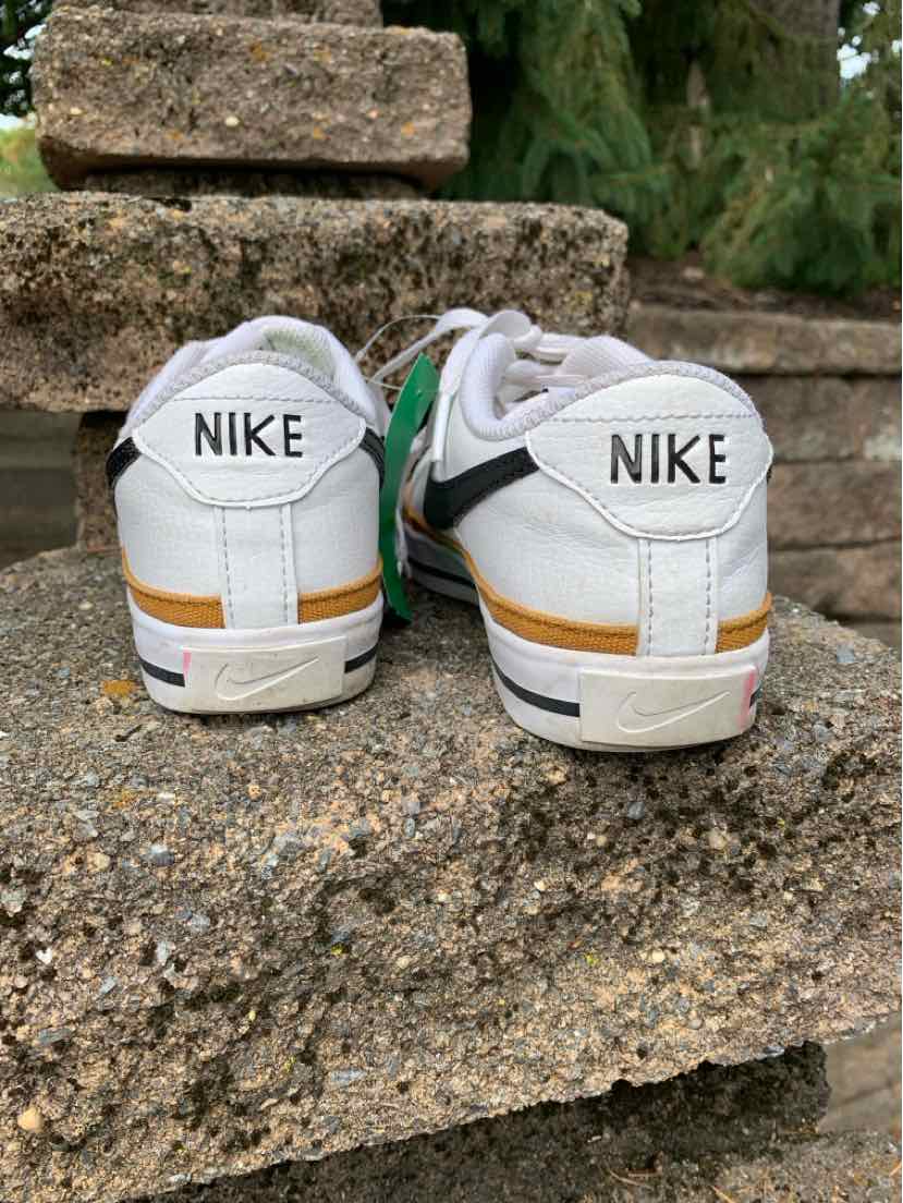 White leather Nike sneakers with black swooshes and gold accents, size 6.5, rear view.