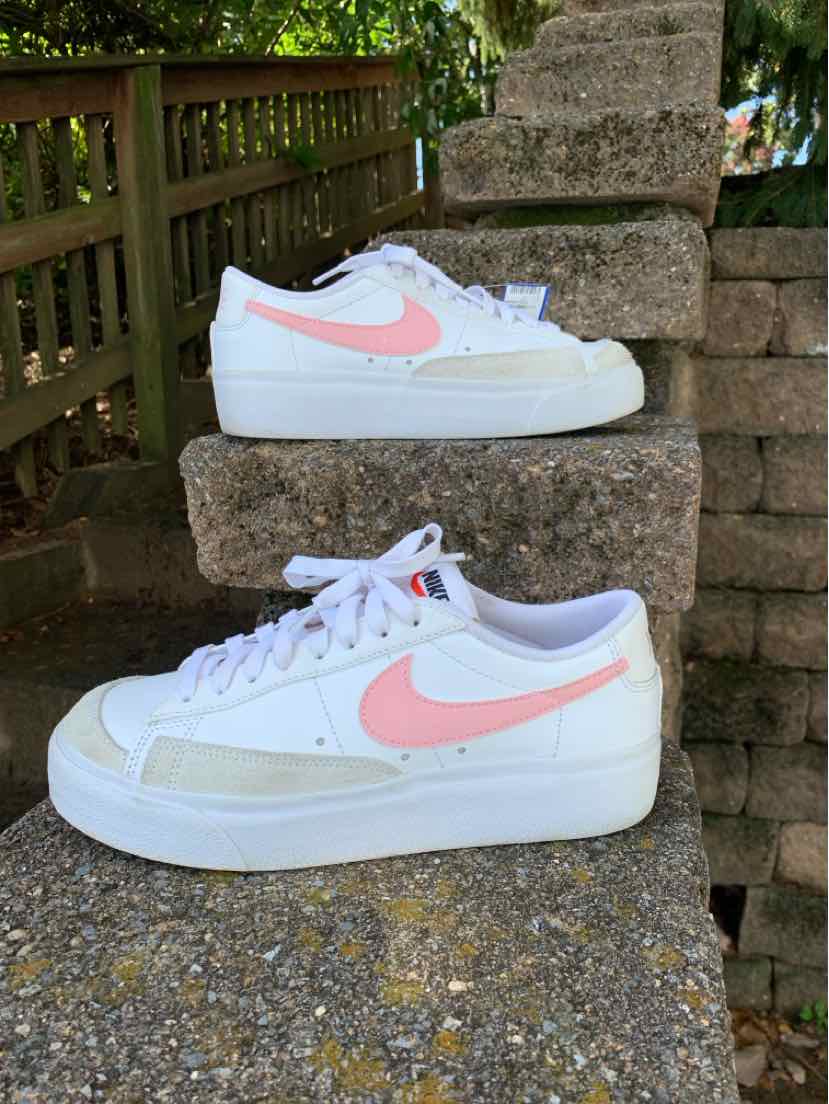 White Nike sneakers with blush pink swooshes, white laces, and pale green side panels, displayed in profile.