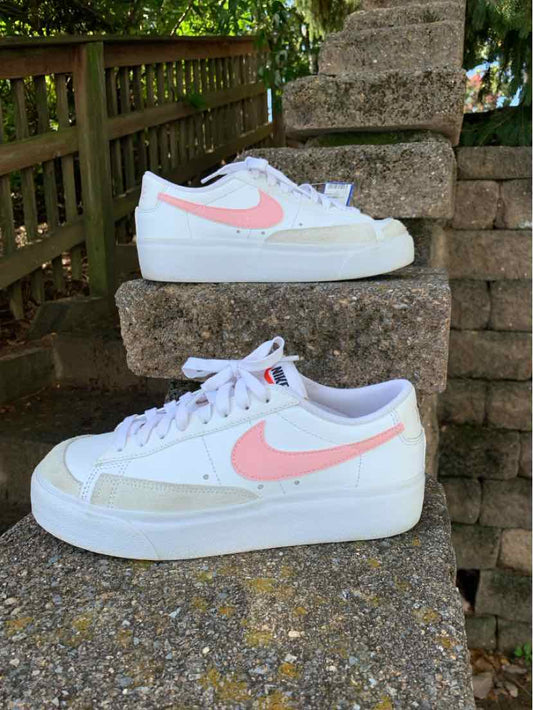 White Nike sneakers with blush pink swooshes, white laces, and pale green side panels, displayed in profile.