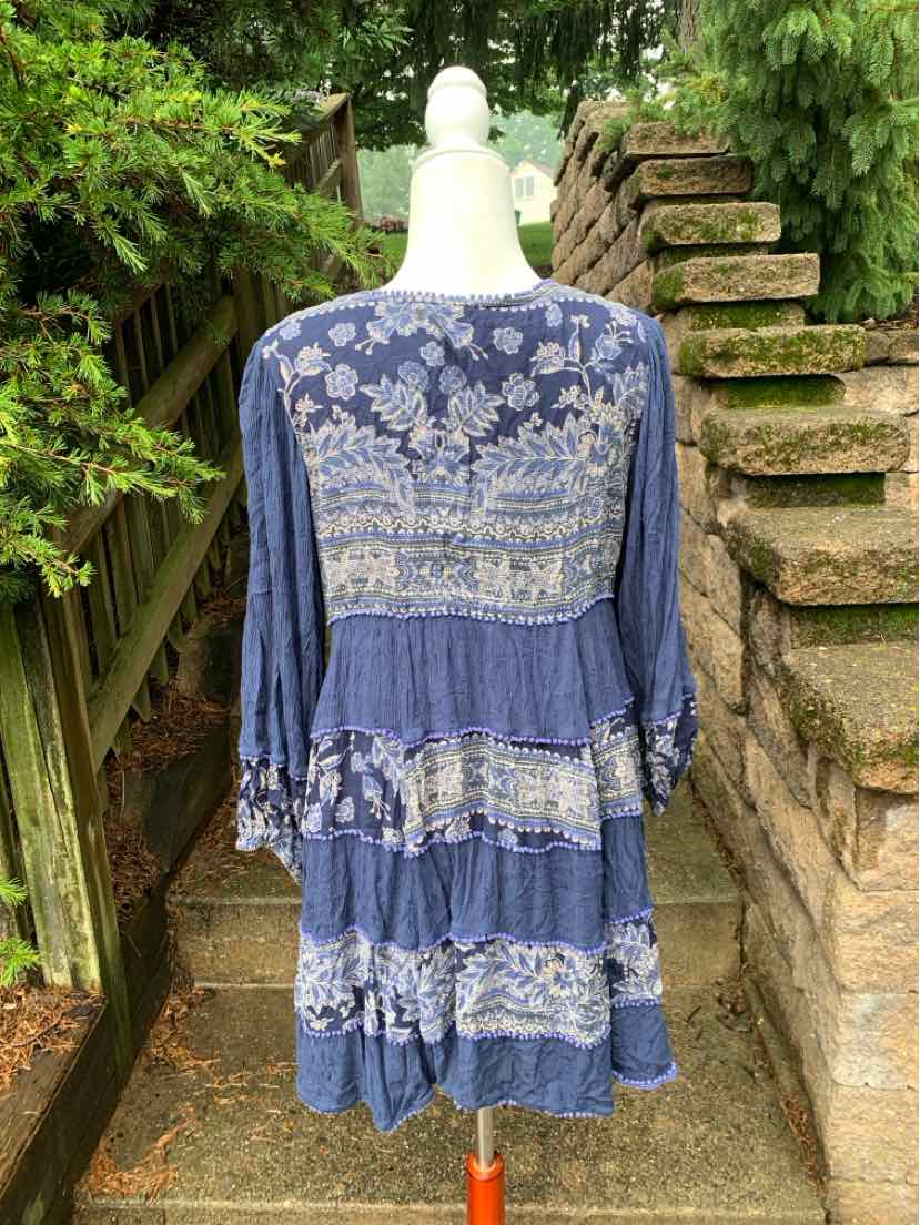 Blue long-sleeve dress with white floral embroidery and tiered ruffle skirt on mannequin outdoors.