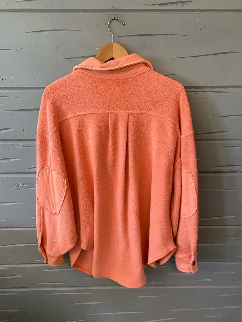 Coral pink long-sleeve shirt with relaxed fit, elbow patches, and a collared neckline hanging on wooden hanger.