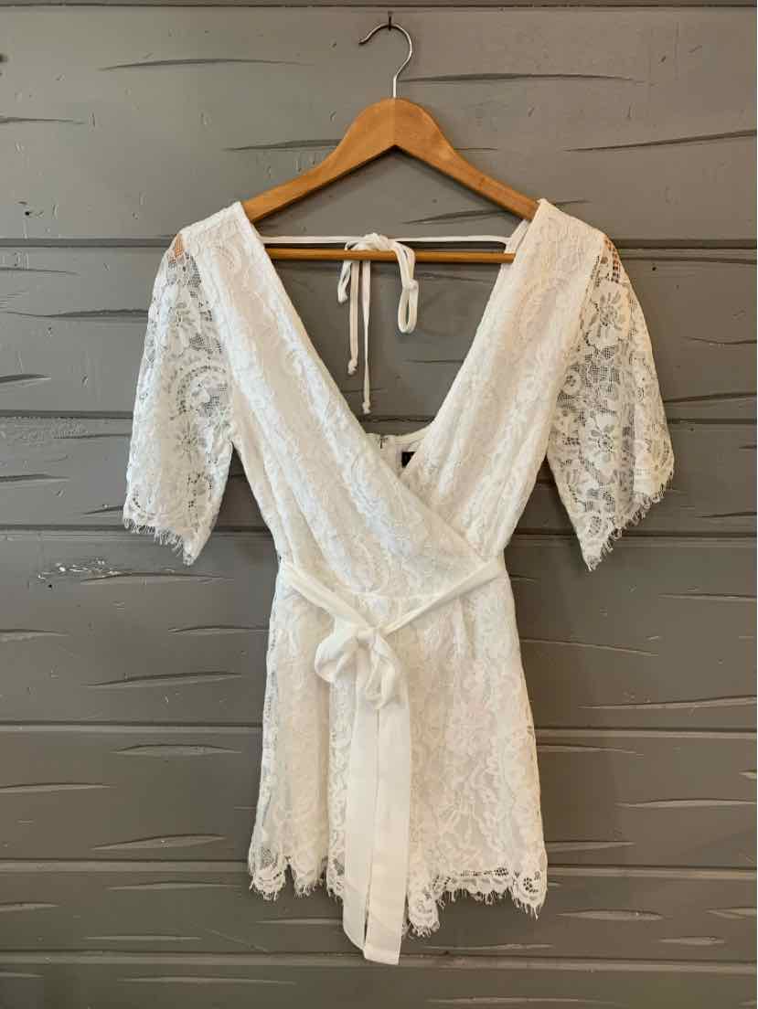 White lace dress with deep V-neck, half sleeves, and waist tie belt on wooden hanger.