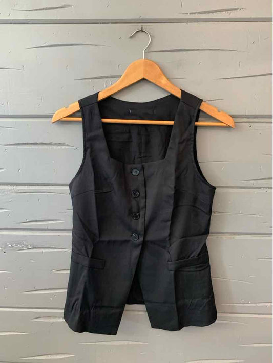 Black sleeveless vest with button front and tailored fit hanging on wooden hanger.