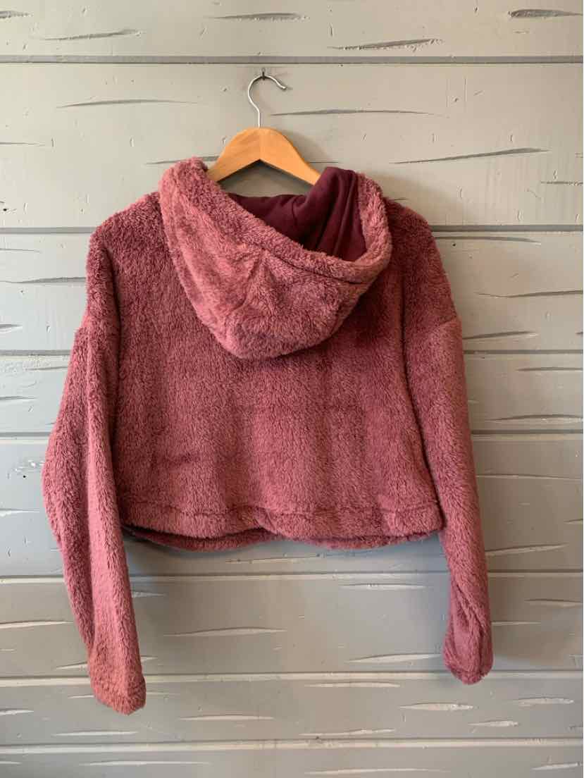 Mauve cropped fleece hoodie with long sleeves and a relaxed fit hanging on wooden hanger against gray wooden wall.