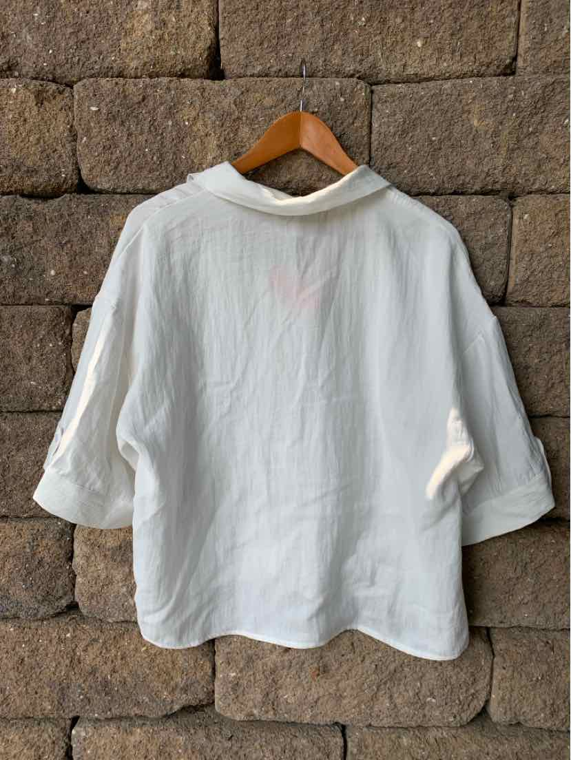 White oversized blouse with three-quarter sleeves and a loose fit hanging on wooden hanger.