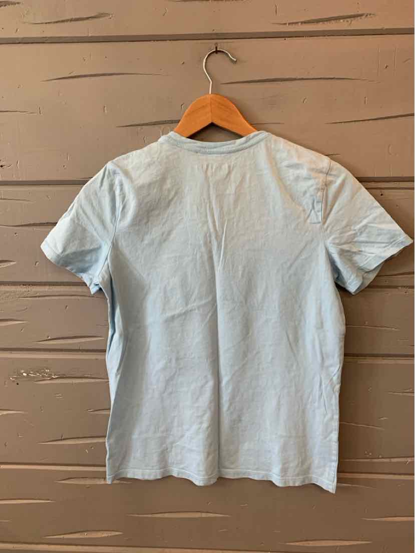 Light blue short-sleeve cotton t-shirt hanging on wooden hanger against wooden wall.