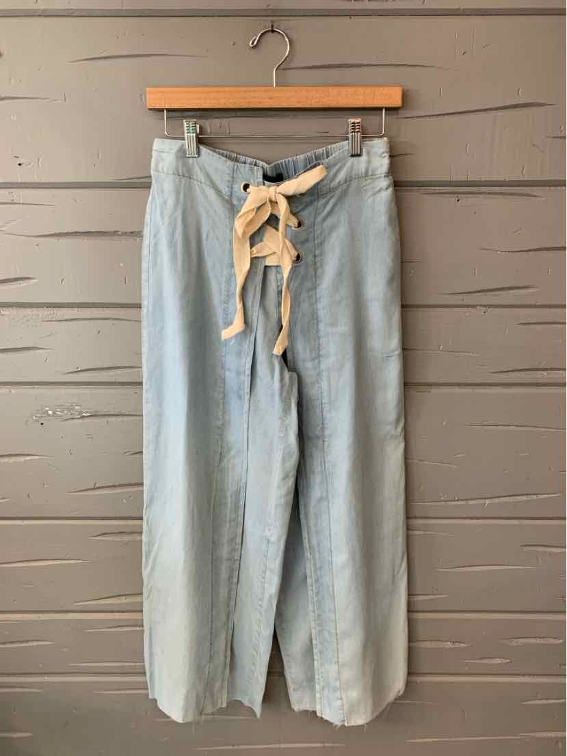 Light blue wide-leg chambray pants with a mustard seed color tie belt hanging on a wooden hanger.