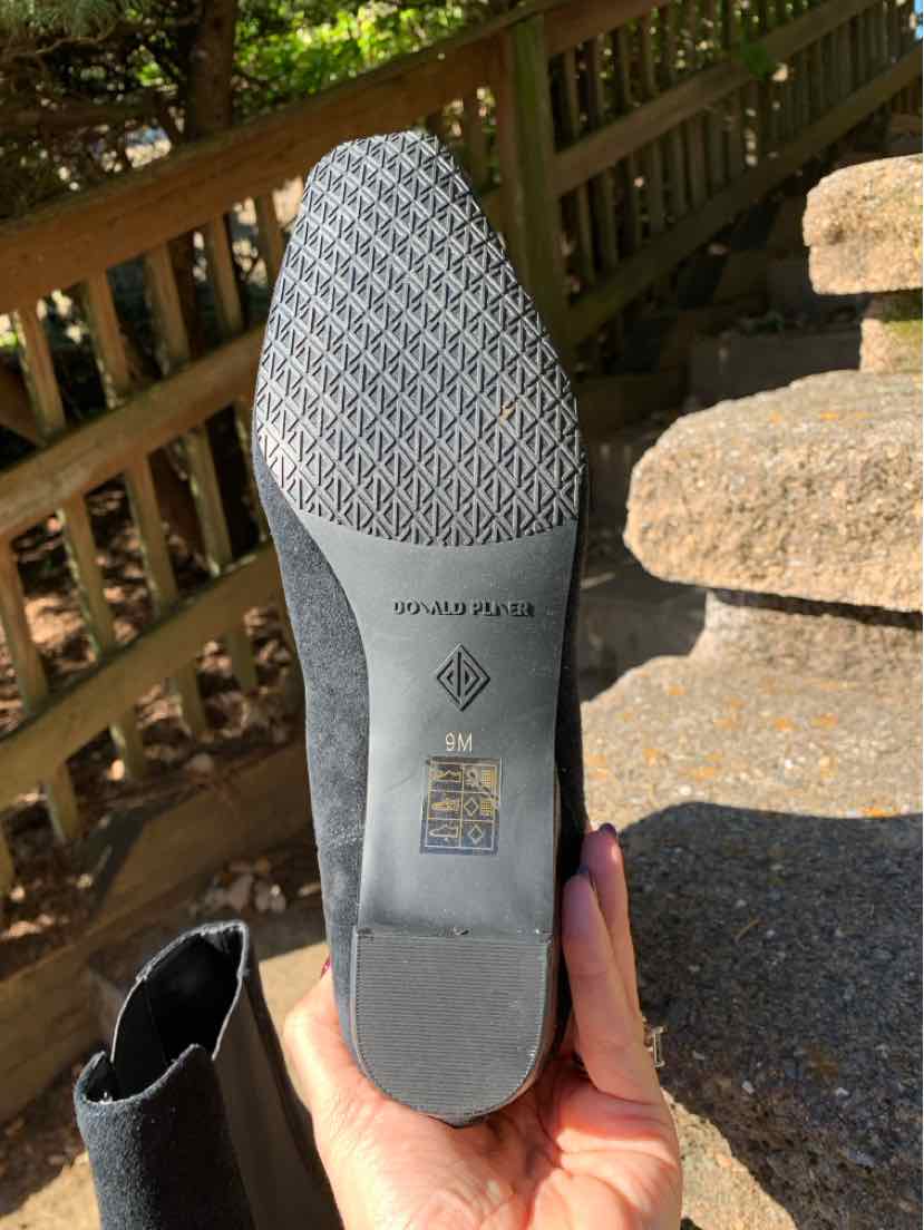 Gray boot outsole with a textured heel and tread, held outdoors; black leather upper peeks into view.