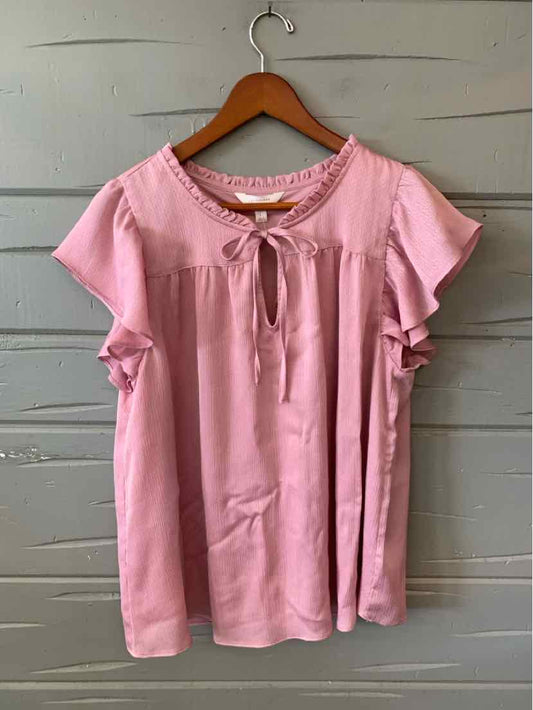 Light pink short-sleeve blouse with ruffled sleeves and keyhole tie neckline hanging on wooden hanger.