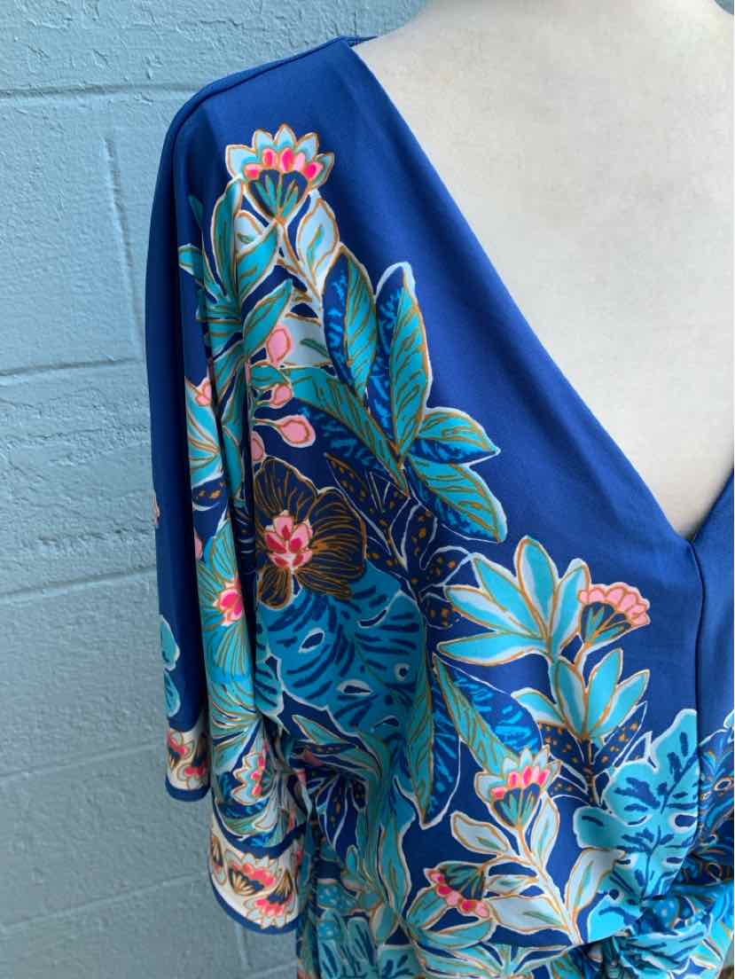 Blue wrap dress with tropical floral print in green, pink, and white, featuring a deep V-neck and flowy sleeves.