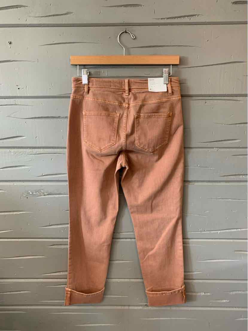 Rust-colored denim pants with a slim fit, back pockets, and rolled cuffs hanging on a wooden hanger.