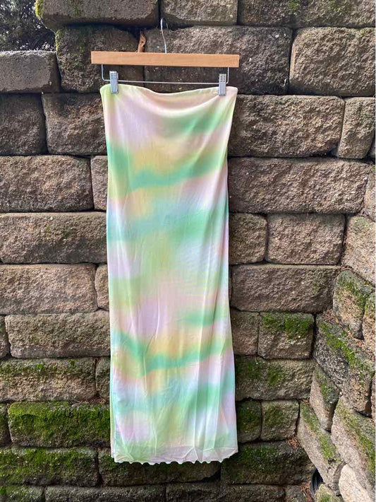 Long pastel multi-color skirt with a ribbed texture and a slightly scalloped hem hanging on a wooden hanger against a stone.